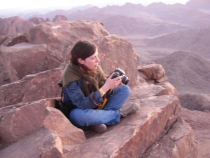 A photo of Daiva Repečkaitė sitting on a cliff, holding a camera