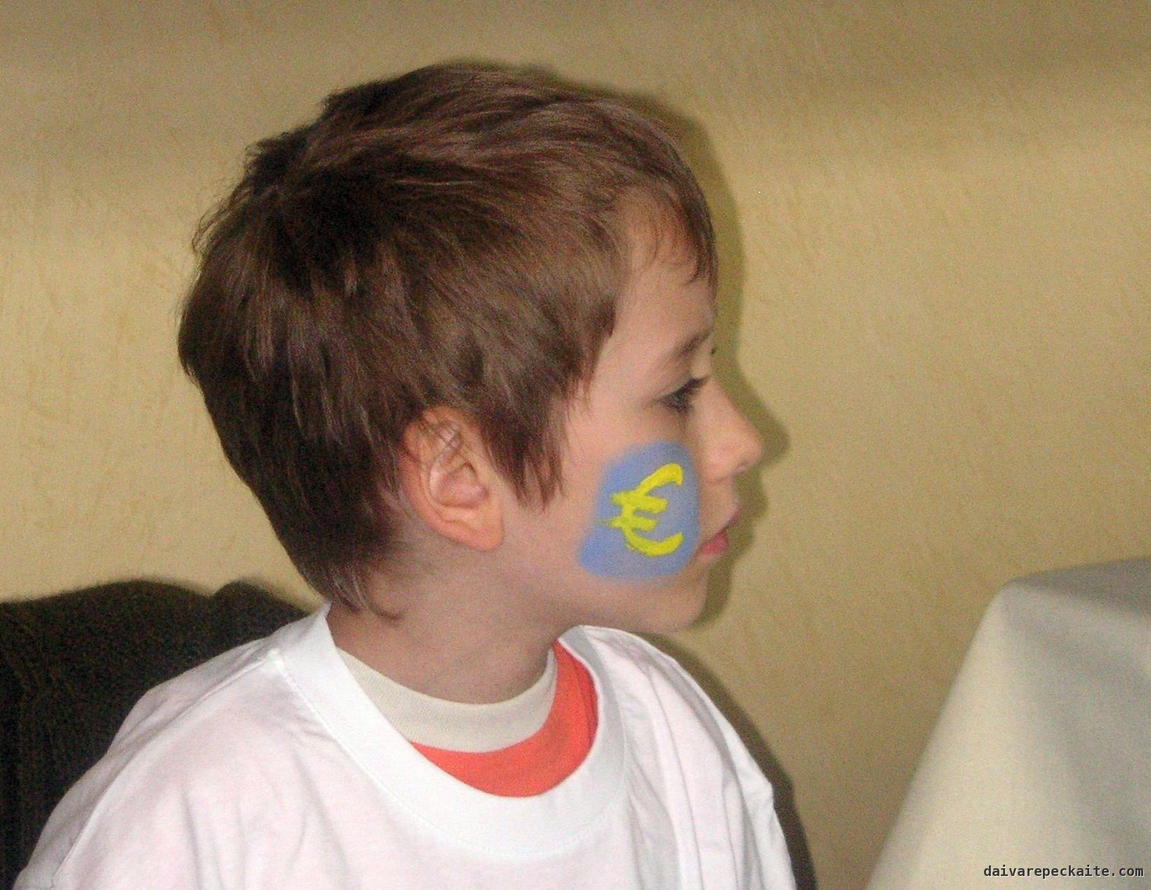 A young child with his face looking sideways and a large euro symbol painted on this cheek