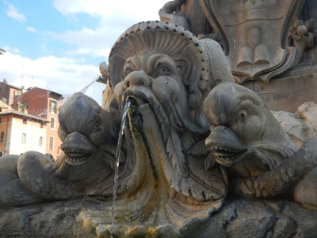 A fountain with a bearded gnome (?) spitting water, flanked by two bird-like characters with teeth in their beaks